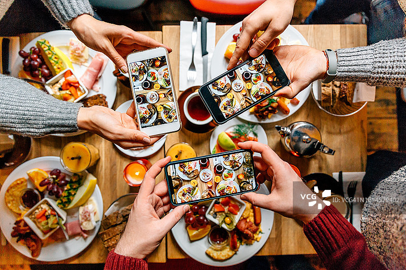 朋友们在餐厅吃早午餐时用智能手机拍桌上的食物图片素材