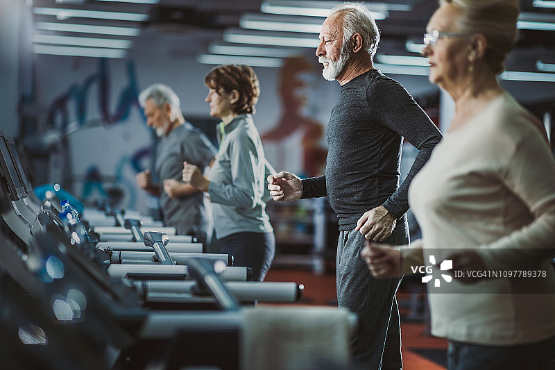 一群活跃的老年人在健身房里的跑步机上跑步。图片素材