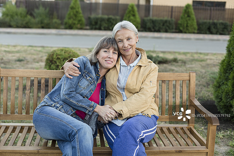 一位年长的女士和她成年的女儿一起坐在长椅上的肖像图片素材