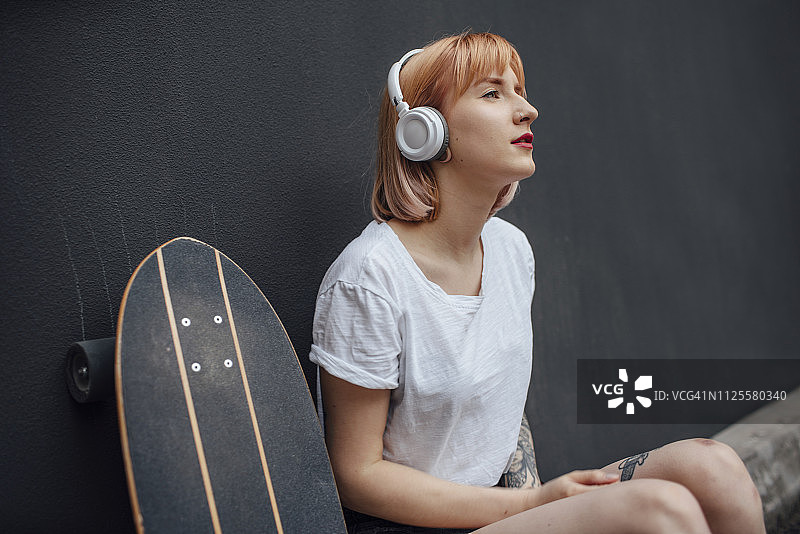 年轻女子带着滑板和耳机听音乐图片素材