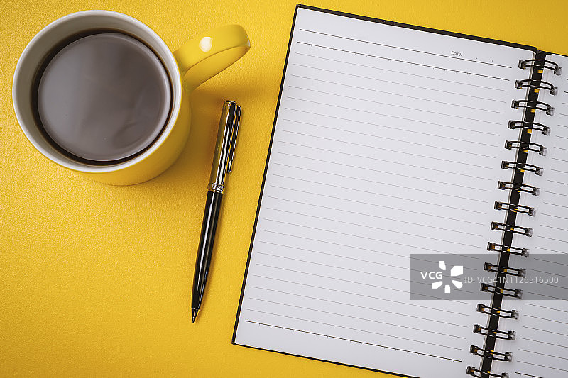 黄色背景上的记事本，钢笔和咖啡杯。图片素材