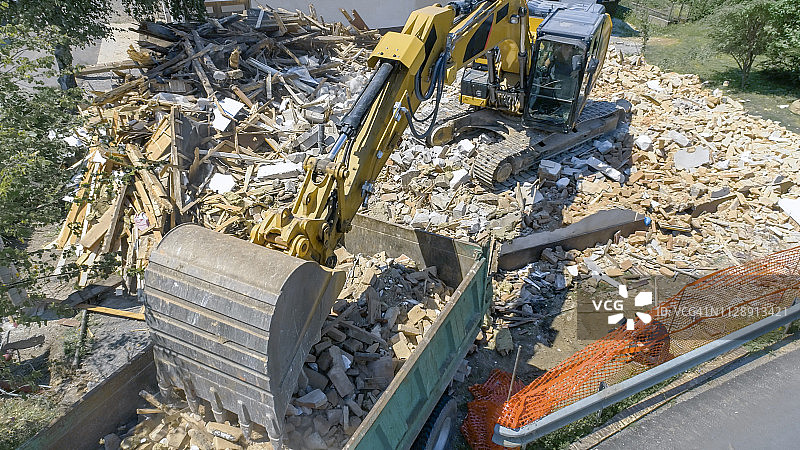 挖掘机将被拆建筑的建筑废料放到卡车上图片素材