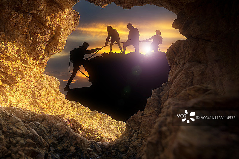 男性和女性登山者攀登悬崖的剪影。从山洞里往外看。图片素材