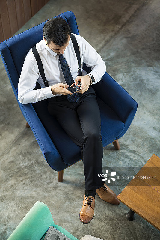 俯视图的商人坐在蓝色的扶手椅上使用智能手机图片素材