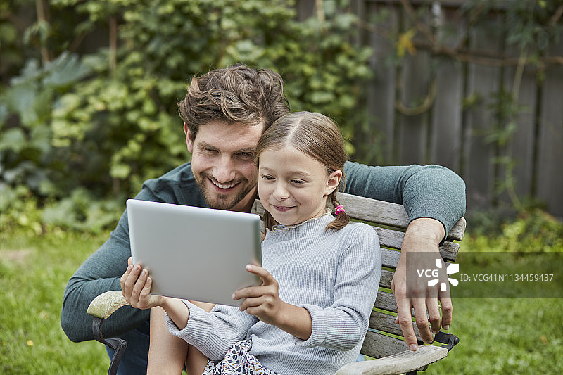 快乐的爸爸和女儿一起在花园里用平板电脑图片素材