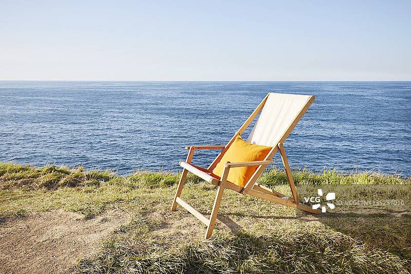 米色帆布躺椅，橙色枕头，草甸上，大海和蓝天图片素材