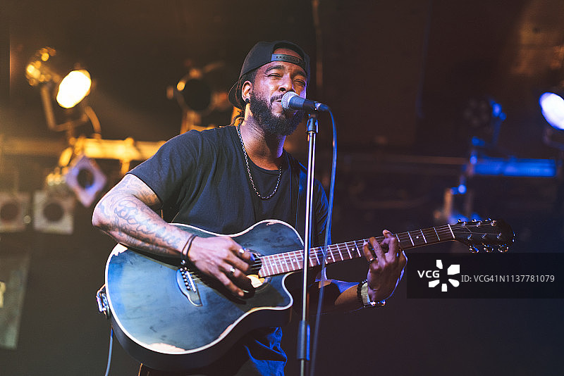 一个黑人弹着原声吉他，在舞台上唱歌图片素材