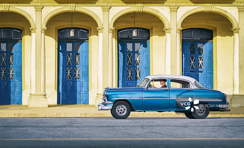 一辆老式的蓝色老爷车穿过古巴哈瓦那老城图片素材