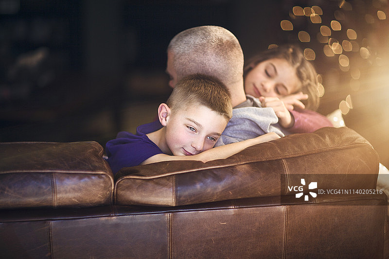 成熟的男人躺在沙发上拥抱着儿子和女儿图片素材