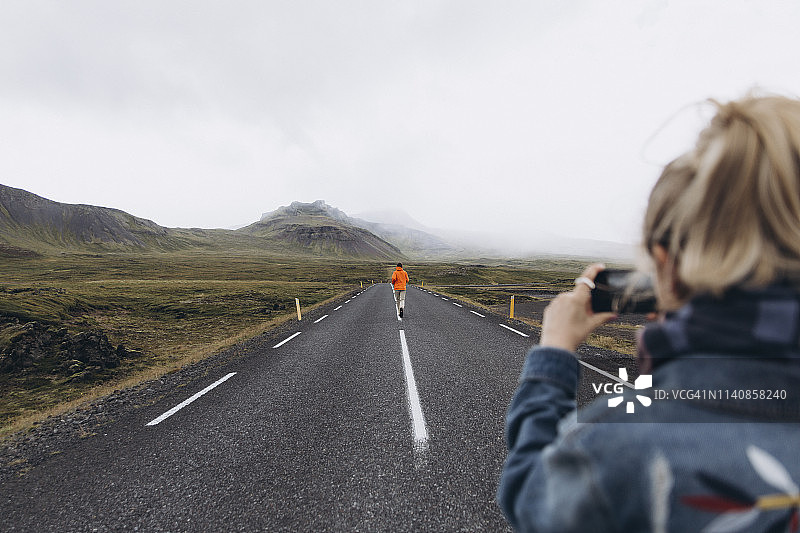 一名年轻女子在冰岛高速公路上给男友拍照图片素材