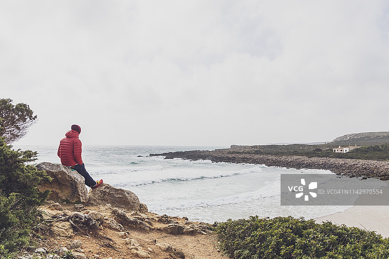 年轻人坐在岩石上，看着波涛汹涌的大海。图片素材