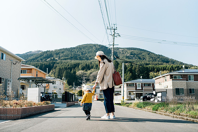 在一个阳光明媚的日子里，母亲和女儿戴着草帽手牵着手走在乡下的小镇上图片素材