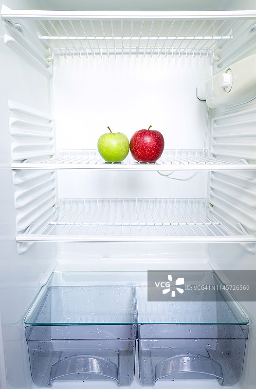 鲜红绿苹果放在打开的空冰箱的架子上。减肥饮食概念。图片素材