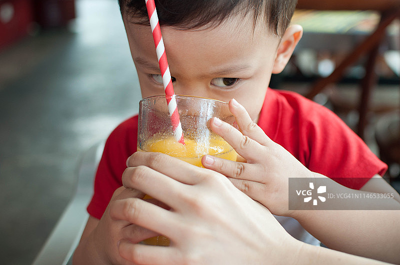 一个小男孩正在用纸吸管喝新鲜成熟的芒果冰沙图片素材