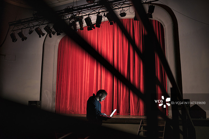 导演站在剧院的舞台前使用笔记本电脑图片素材