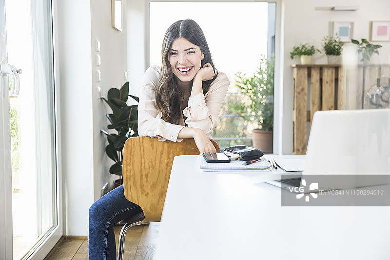 一个快乐的年轻女人坐在家里的桌子旁图片素材