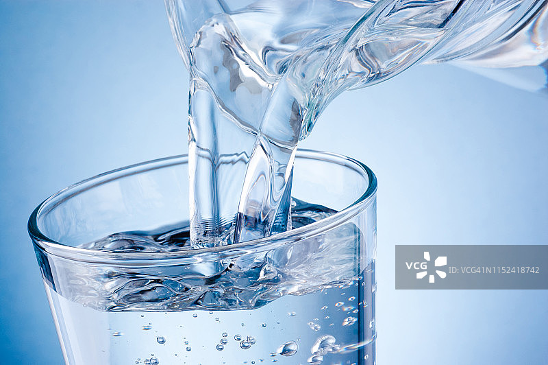 将水从水罐倒入蓝色背景的玻璃杯中图片素材