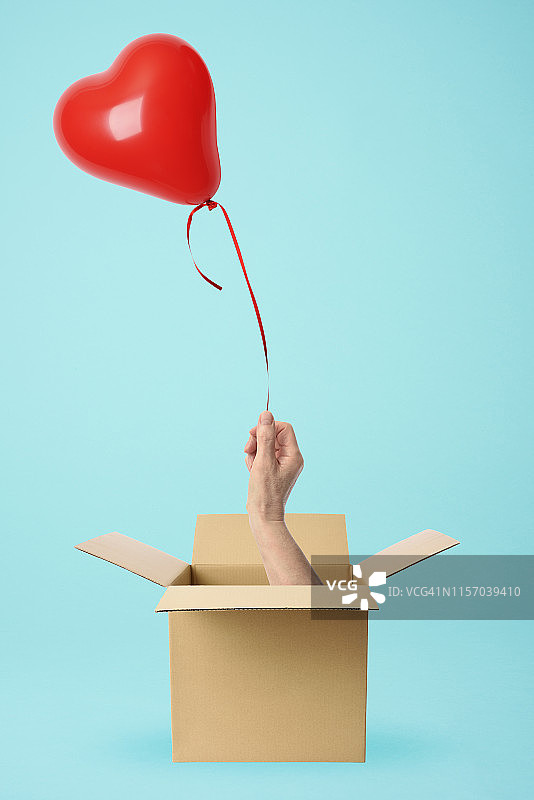 一只手从纸板盒里拿着一个红色的心形气球图片素材