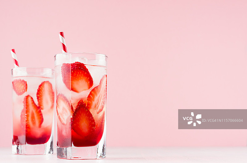 夏日冷草莓自制柠檬汁配熟透的浆果片，冰，稻草在柔和的浅粉色背景，白色的木桌上。图片素材