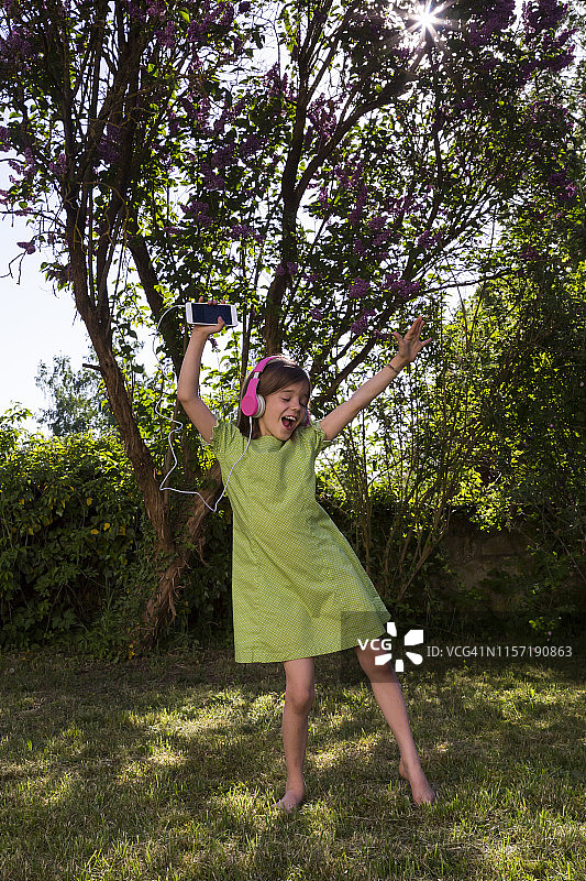 戴着耳机和智能手机的唱歌女孩在花园里跳舞图片素材