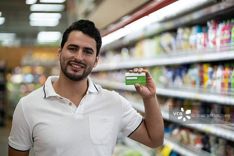 一个年轻人在超市拿着奖励卡，对着镜头微笑图片素材