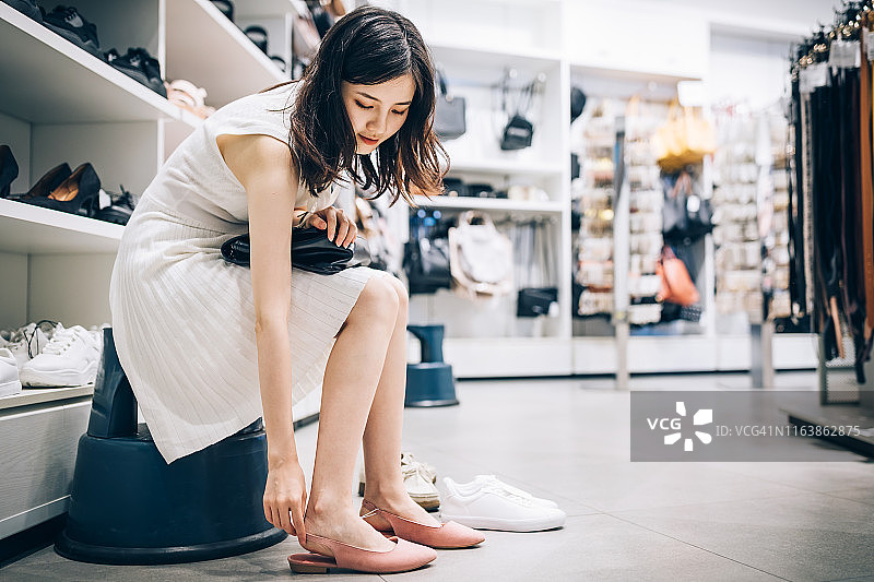 年轻的亚洲妇女在鞋店试穿一双新凉鞋。图片素材