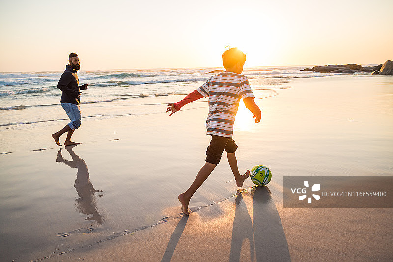 爸爸和儿子在沙滩上踢足球图片素材