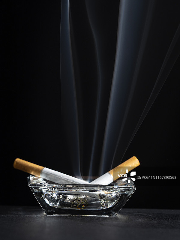 黑色背景上的烟灰缸内点燃的香烟有烟迹。图片素材