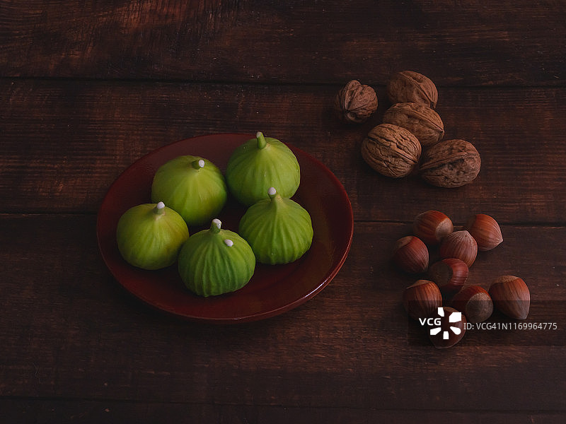 秋天的水果:一组新鲜采摘的绿色无花果放在粘土盘子里，坚果和榛子放在旧的深色木桌上图片素材