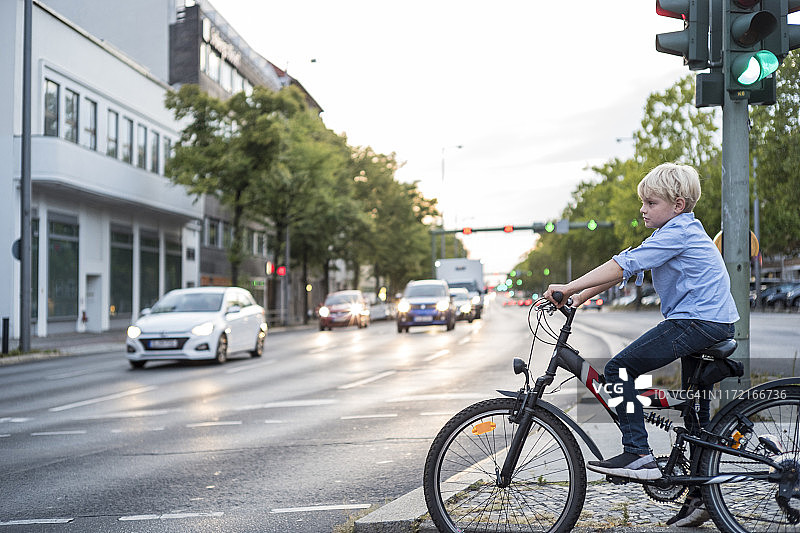 一个骑着自行车的男孩正在一条大马路的红绿灯前等待图片素材