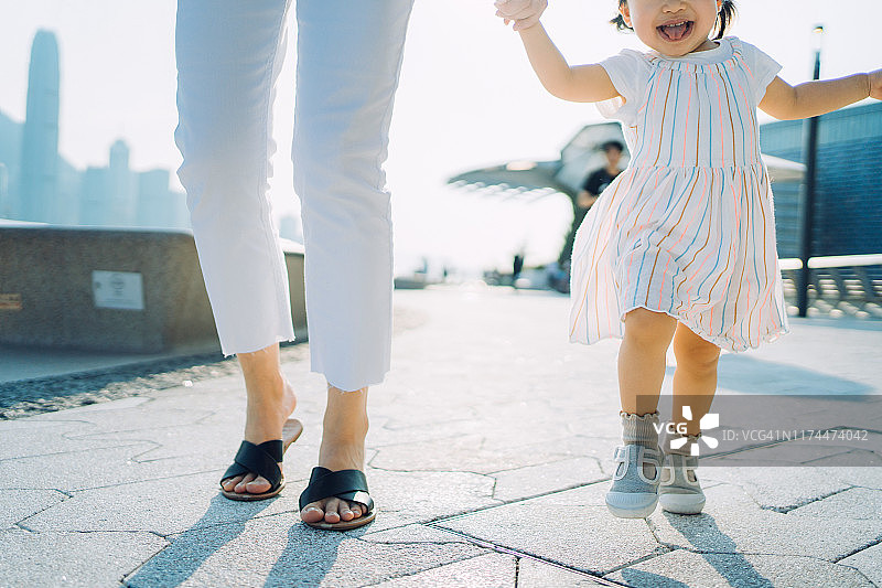 近距离拍摄母亲牵着可爱的小女儿在散步，面带微笑图片素材