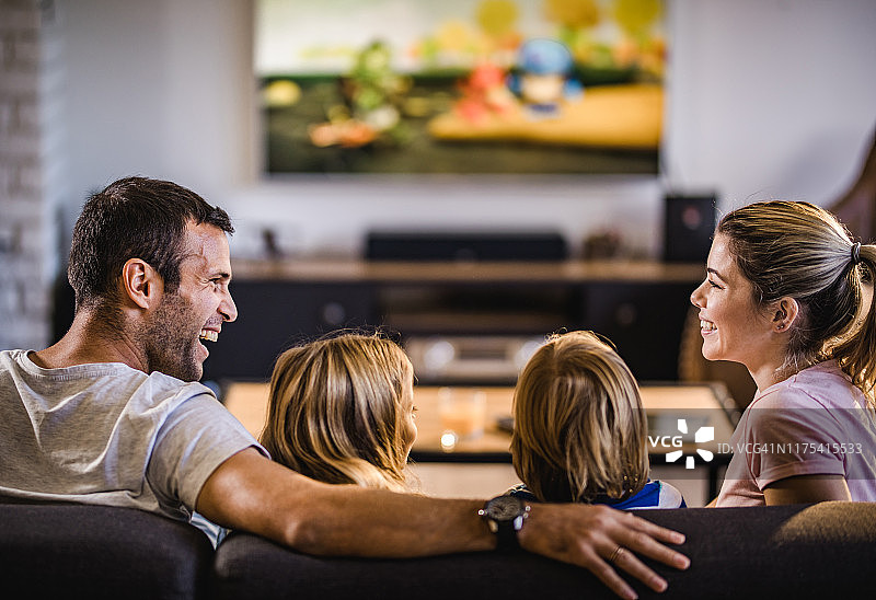快乐的父母在家里和孩子们一起看电视的时候聊天。图片素材