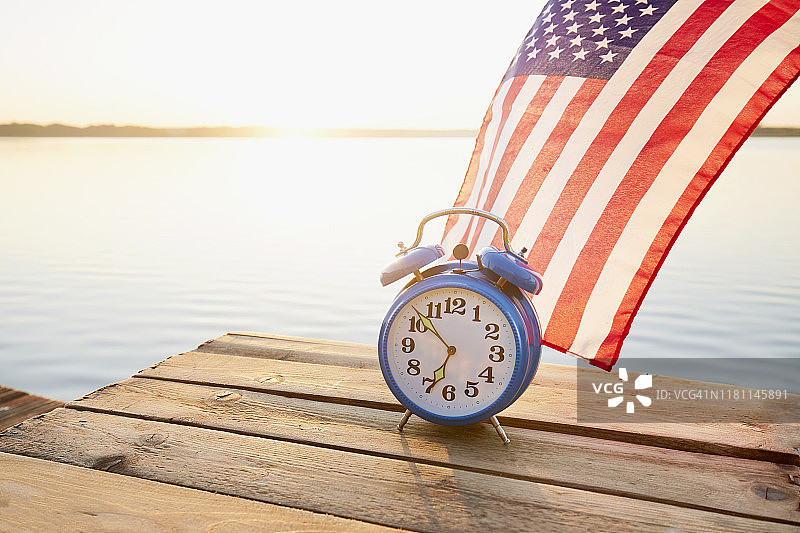 在日出的清晨，复古闹钟和美国国旗在湖边的码头上图片素材
