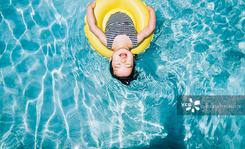 高角度的可爱的亚洲学步女孩闭上眼睛，而浮动与一个充气环放松在游泳池图片素材