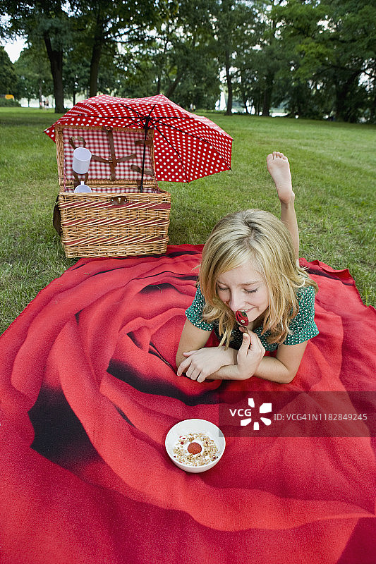 一个女孩拿着一碗酸奶，格兰诺拉麦片和草莓在野餐图片素材
