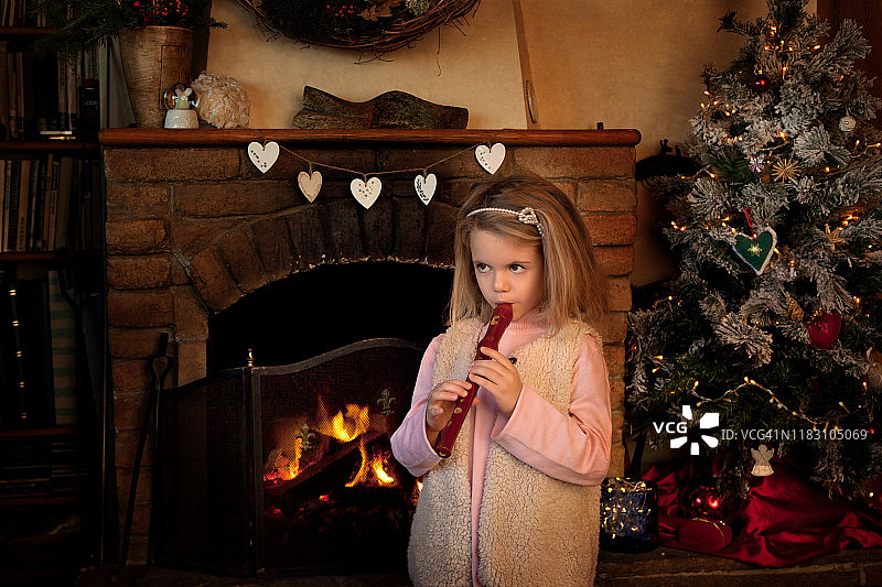 圣诞节的时候，一个女孩站在壁炉前吹着录音机图片素材