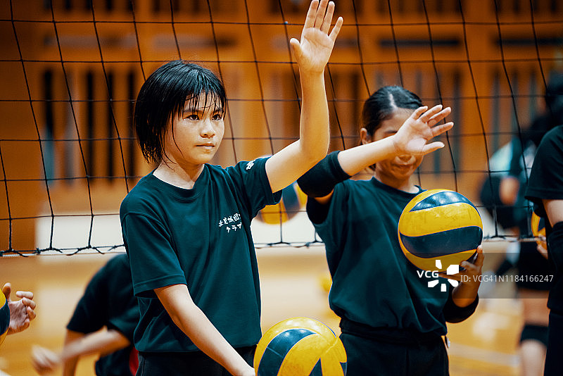 在学校体育馆里，一个小女孩在集体排球练习中扣球图片素材