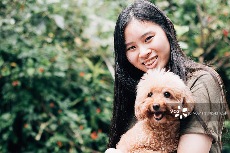 亚洲少女的肖像与宠物贵宾狗微笑面对前面图片素材
