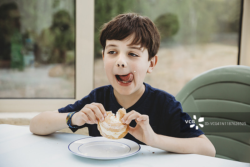 男孩的肖像，奶油甜甜圈舔他的脸颊上的奶油图片素材