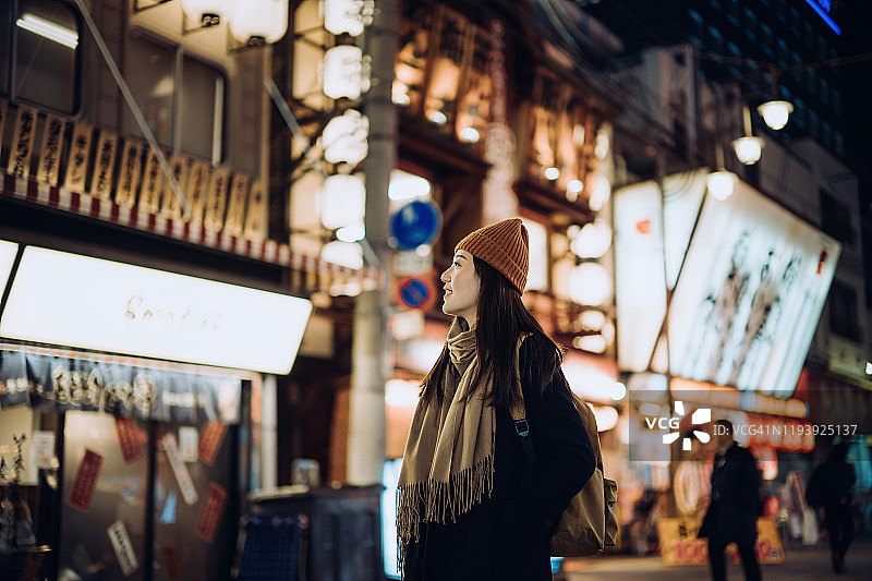 微笑的年轻亚洲女性旅行者探索和漫步在繁忙的当地城市街道晚上在大阪，日本图片素材