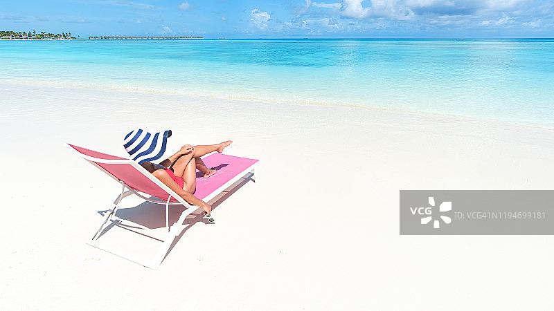 年轻美丽的女人放松躺在太阳太阳躺椅附近的海-夏季海滩度假概念图片素材