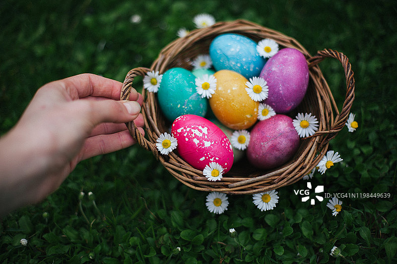 前面集中了年轻女子的手拿着篮子，上面有五颜六色的复活节彩蛋在绿色的草地上图片素材