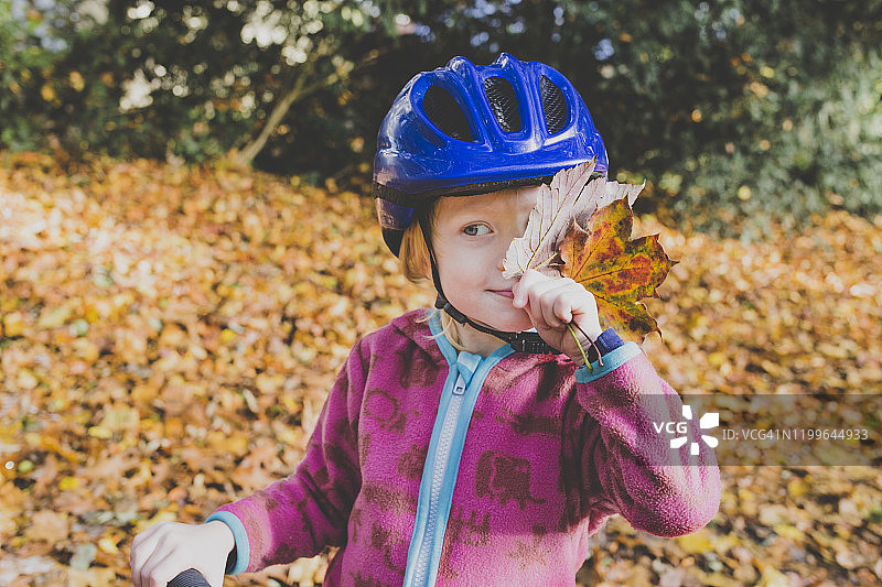 小女孩的肖像与秋天的树叶戴着蓝色的自行车头盔图片素材
