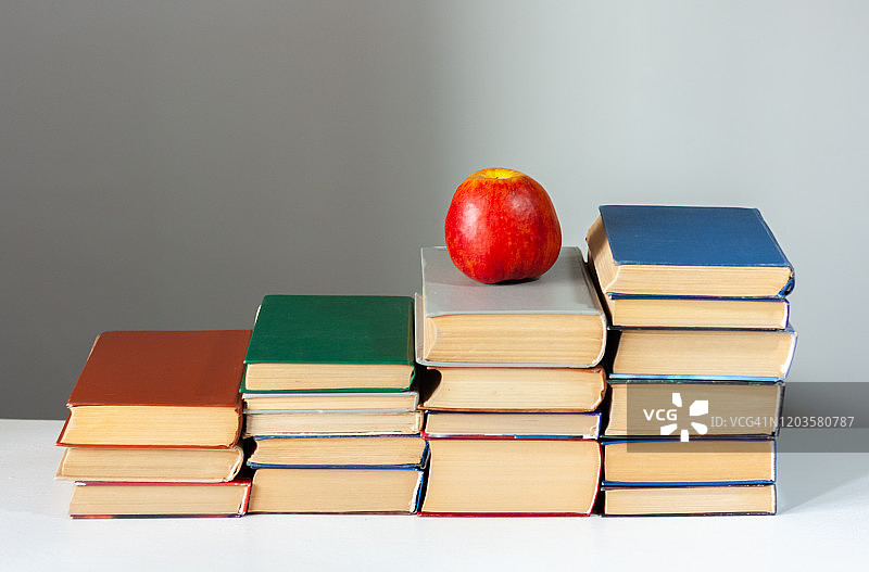 白色的桌子上放着红苹果，上面放着精装书。书堆积。回到学校的概念。副本的空间。教育学习背景图片素材