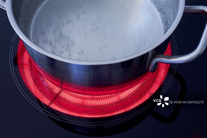 高角度的水壶与沸腾的水在一个加热的陶瓷炉顶图片素材