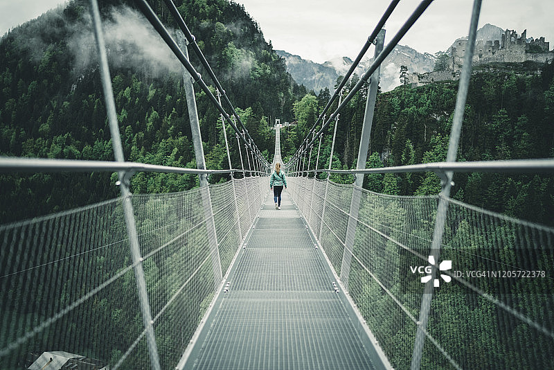 年轻女性徒步穿越高山环境中的吊桥图片素材