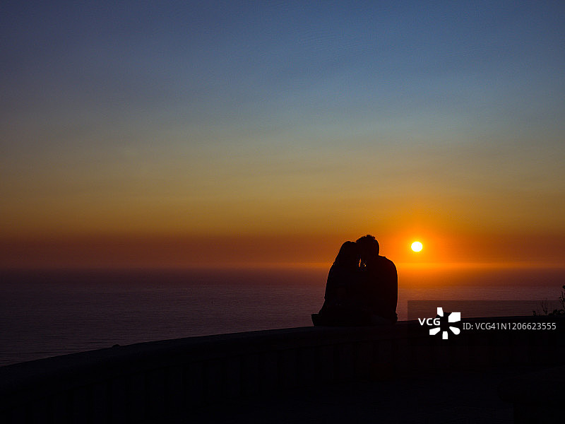 一对夫妇的背影剪影看日落与海的背景在夏季与温暖的光图片素材