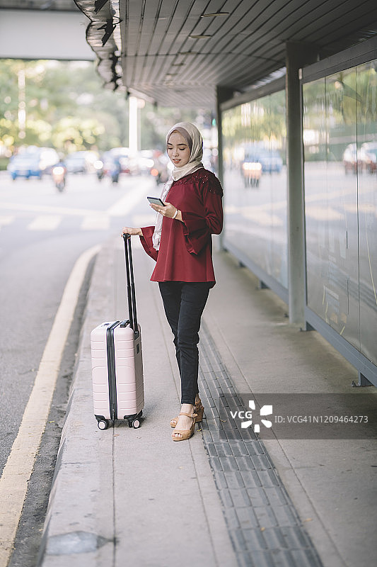 一名亚洲现代穆斯林妇女手持行李在吉隆坡的公交车站等待运输图片素材