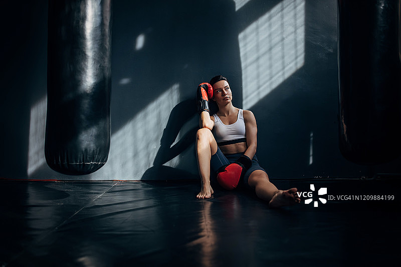 疲惫的年轻女子拳击手坐在地板后，练习和休息图片素材