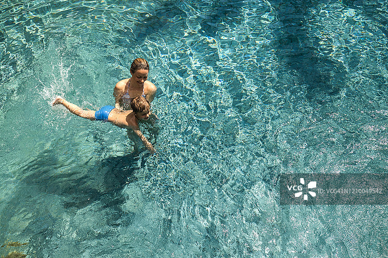 上图是一位快乐的单身母亲教她的儿子在游泳池里游泳。图片素材